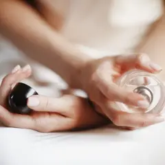 Dłonie kobiety trzymające flakonik perfum i czarny korek.